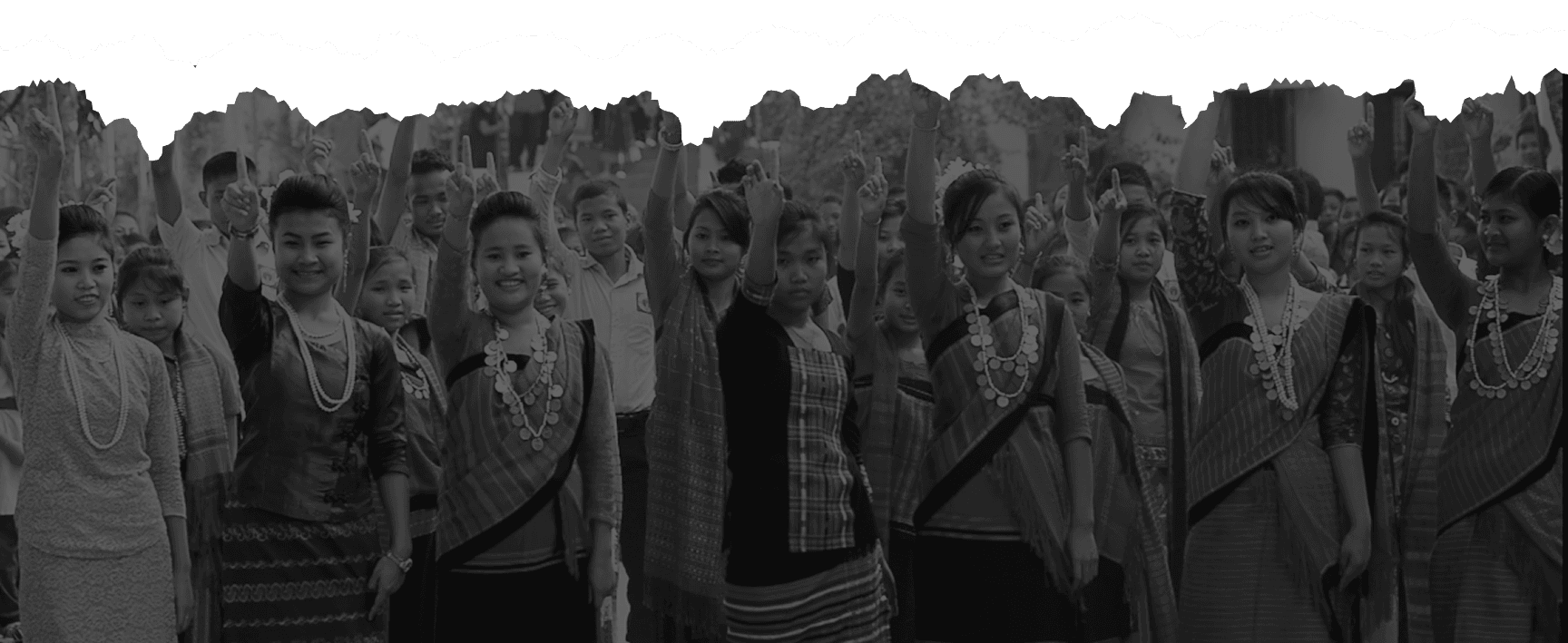 A crowd of indigenous women and young people in traditional dress raising a finger in pledge, Rangamati.